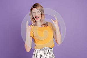 Photo of young woman showing rock sign and screaming having fun isolated over violet color background