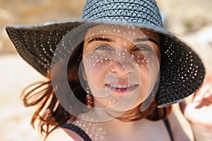 Photo of a young woman in swimsuit and a blue big hat smiling and sunbathing on the beach