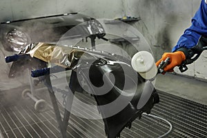 The photograph captures the scene of an automotive workshop, showcasing the process of painting various car parts.