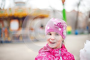 A photograph of a child`s rest on nature in the spring. A child girl in a bright pink jacket is eating sweet cotton wool against t