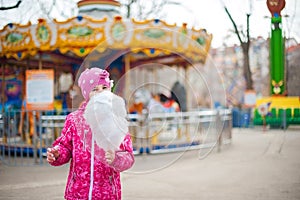 A photograph of a child`s rest on nature in the spring. A child girl in a bright pink jacket is eating sweet cotton wool against t