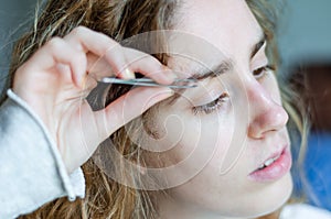 Photograph of a girl plucking her eyebrows with tweezers.