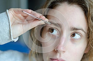 Photograph of a girl plucking her eyebrows with tweezers.