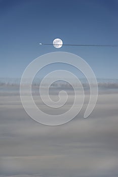 Air plane flies through a full moon way above the clouds.