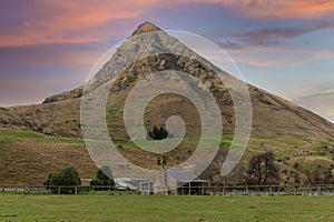 Photograph of an old farm cottage in front of a large hill in New Zealand
