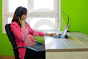 photograph of pregnant woman working in her office with laptop and headphones. copy space