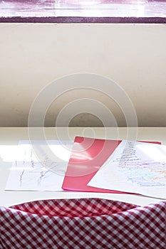 Photograph of some drawings and a red folder of a child on a table in a classroom of a nursery school.The photo is shot in