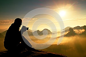 Photograph takes photos of daybreak above heavy misty valley. Landscape view of misty autumn mountain hills and happy man silhoue