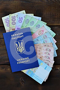 A photograph of a Ukrainian passport and a certain amount of Ukrainian money on a wooden surface. The concept of making money for