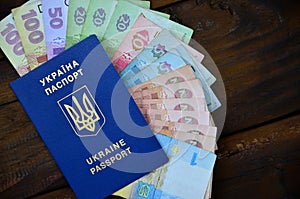 A photograph of a Ukrainian passport and a certain amount of Ukrainian money on a wooden surface. The concept of making money for