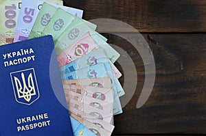 A photograph of a Ukrainian passport and a certain amount of Ukrainian money on a wooden surface. The concept of making money for