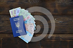 A photograph of a Ukrainian passport and a certain amount of Ukrainian money on a wooden surface. The concept of making money for