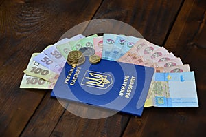 A photograph of a Ukrainian passport and a certain amount of Ukrainian money on a wooden surface. The concept of making money for