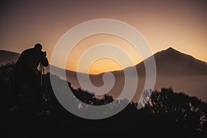 Photographer in action in scenery sunset with high mountain in background and orange colors around -wild active people enjoyin the