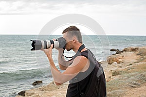A photographer with a backpack on the cliff taking pictures of the sea.