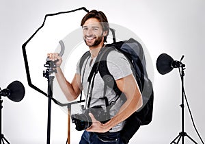Photographer, backpack and happy with camera in studio for career, behind the scenes and equipment. Photography, person