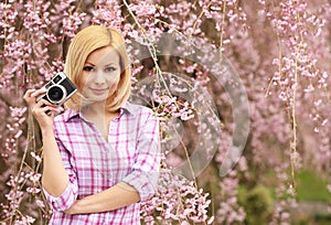 Photographer. Blonde Girl with Retro Camera over Cherry Blossom.