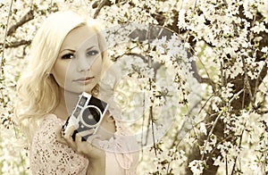 Photographer. Blonde Woman with Retro Camera over Cherry Blossom