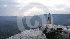 Photographer in blue jacket stand on rocky view point and taking photos of misty morning landscape. Hike in rocks.