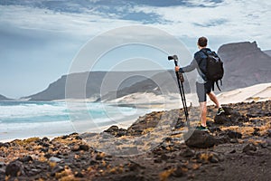 Photographer with camera on tripod in desert admitting unique landscape of sand dunes volcanic cliffs on the Atlantic