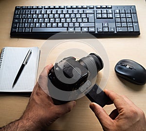 Photographer checking the camera with keyboard, mouse, and notebook on a desk