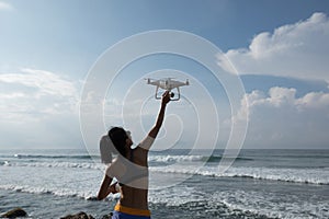 Photographer controlling a flying drone on seaside rock