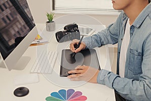 Photographer drawing and retouching image on laptop computer, using a digital tablet and stylus pen. Closeup of man`s hand with