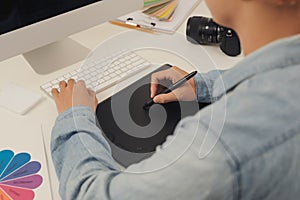Photographer drawing and retouching image on laptop computer, using a digital tablet and stylus pen. Closeup of man`s hand with