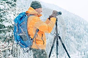 Photographer dressed orange softshell jacket with backpack making a landscape shoot using a digital camera and tripod while he