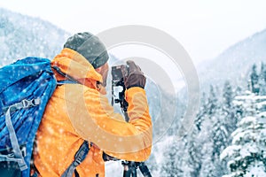 Photographer dressed orange softshell jacket with backpack making a landscape shoot using a digital camera and tripod while he photo