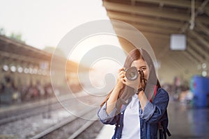 Photographer girl smile holding digital camera. Young Asian woman traveler with camera taking pictures on subway train platform.