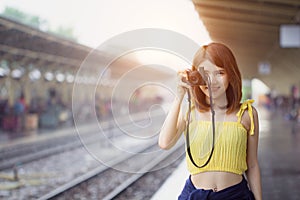 Photographer girl smile holding digital camera. Young Asian woman traveler with camera taking pictures on subway train platform.