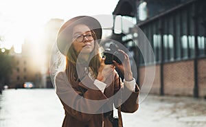 Photographer in glasses with retro camera take photo in city. Tourist smiling girl in hat travels in Barcelona holiday. Sunlight