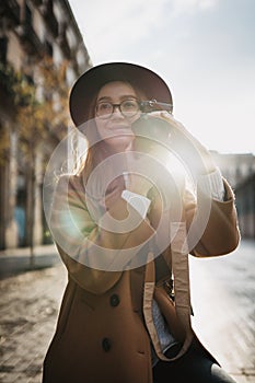 Photographer in glasses with retro photo camera. Tourist portrait. Girl in hat travels in Barcelona holiday. Sunlight flare street