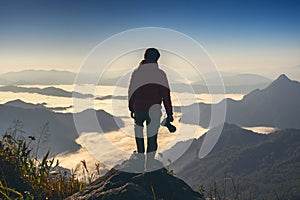 Photographer hand holding camera and standing on top of the rock in nature. Travel concept