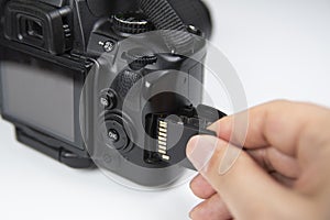 Photographer hand holding SD memory card insert DSLR camera.