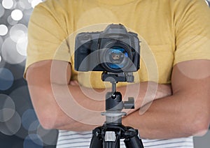 photographer hands folded with camera with tripod in front. Silver bokeh behind