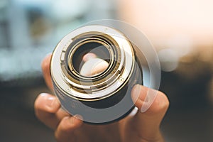 Photographer is holding a photography lens in his hand, laptop in the blurry background