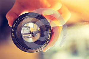 Photographer is holding a photography lens in his hand, laptop in the blurry background