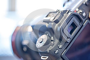 Photographer holds a reflex camera with telephoto lens in his hand. Table and laptop in the blurry background