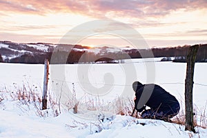 Photographer lay in snow on meadow and takes a picture of fantastic sunset above hill