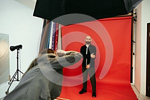 Photographer makes a photo shoot for a handsome bearded man on a red background in a photo studio