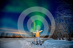 Photographer man with camera and tripod photographs aurora borealis, northern lights green. Concept photo tour to arctic