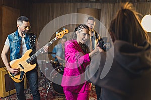 Photographer recording music video clip of a band. Indoor shot of female vocalist, male drummer, and male guitarist in