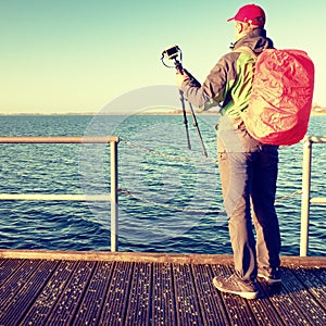 Photographer with red backpack on wooden pier above sea