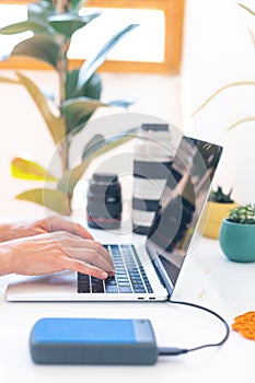 Photographer`s workplace, laptop and camera lenses on a white table, hands on keyboard close up