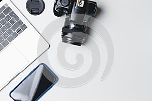 Photographer`s workplace on a white background. Modern laptop, digital camera, lens, battery, smartphone. Minimalism. Top view