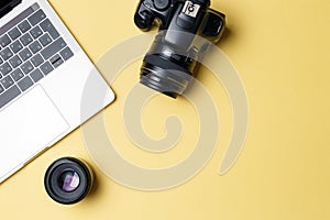 Photographer`s workplace on a yellow background. Modern laptop, digital camera, lens, battery, smartphone. Minimalism