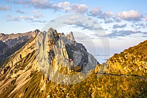 A photographer shooting the colorful sunrise on the steep ridge of the majestic  Schaefler peak in the Alpstein mountain range