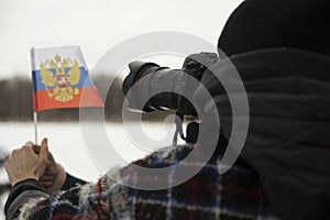 Photographer shoots flag of Russia. Small flag in hand